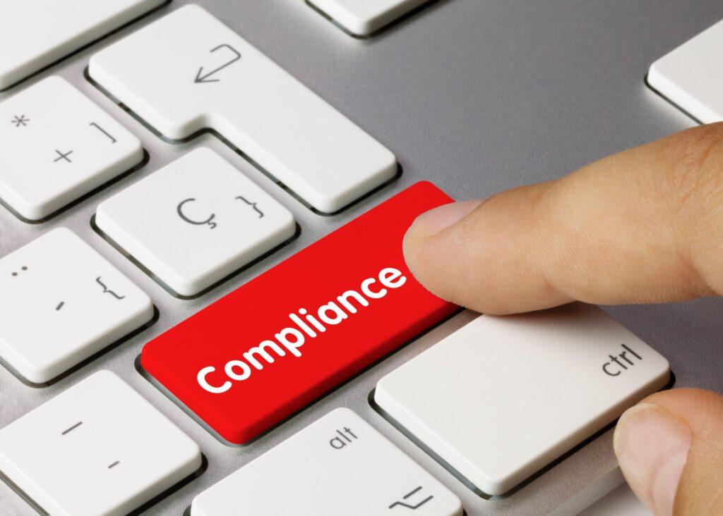 A business owner presses a red button on a white keyboard that says “compliance.”